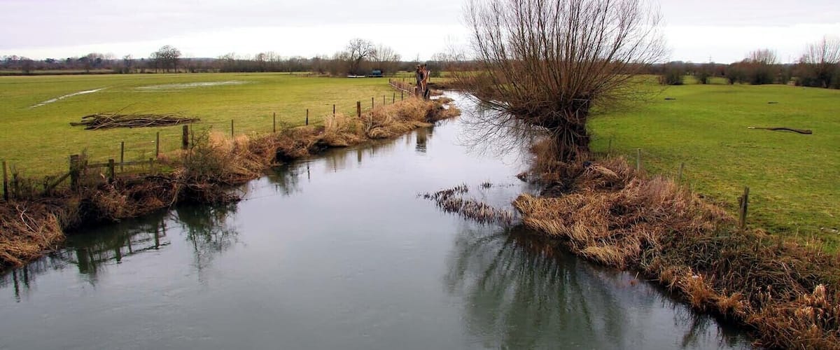 A narrow water channel with a fence on one side and a grassy field on the other.