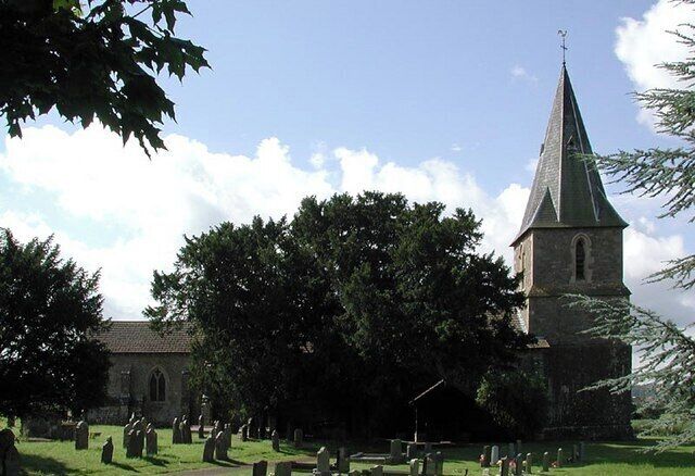 A church with a tall steeple, surrounded by trees and a cemetery.