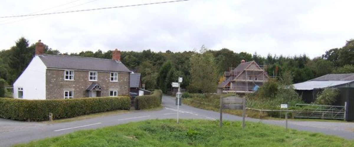 A rural road with a house on the left, a construction site on the right, and a signpost in the middle.