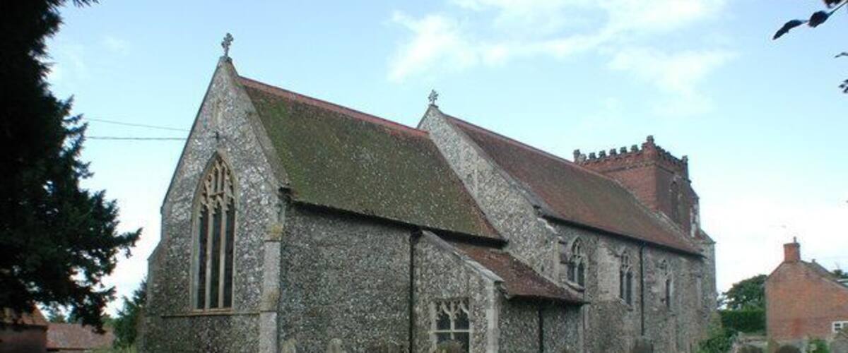 A stone church with a steep roof and a large arched window, surrounded by a cemetery with headstones.