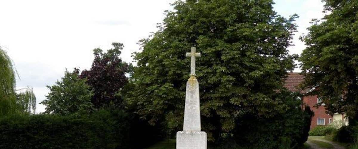 A white cross monument with steps, surrounded by grass and trees.