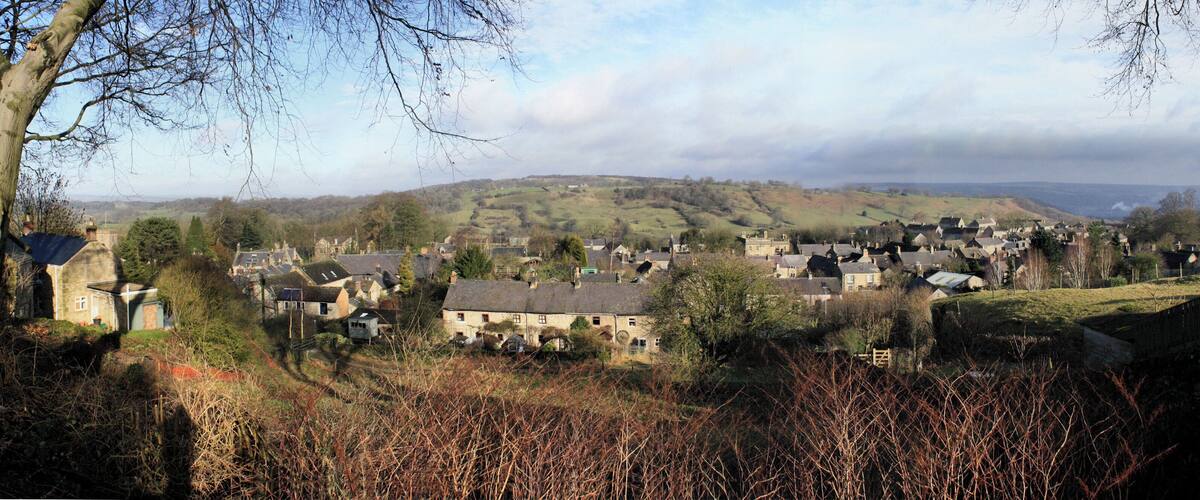 A village with houses on a hillside, surrounded by trees and open fields.