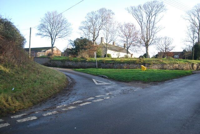 A rural road with a sharp bend, stone walls, and houses in the background.