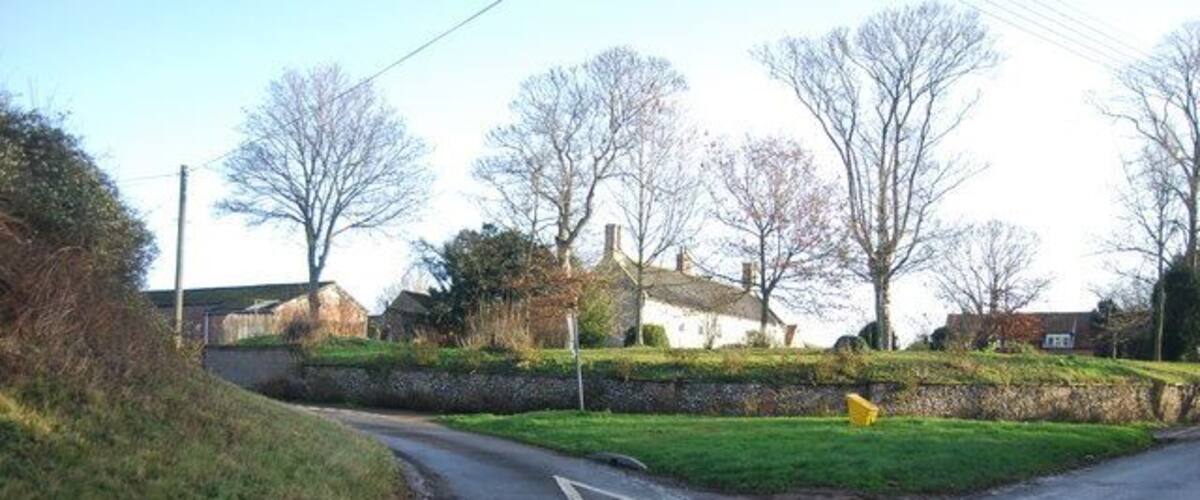 A rural road with a sharp bend, stone walls, and houses in the background.