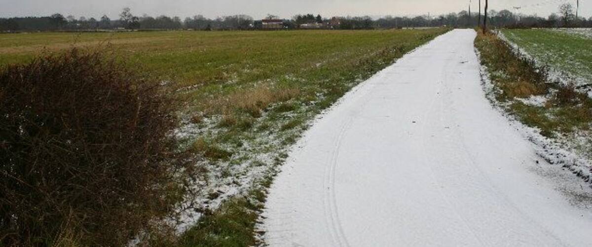 A snow-covered rural road flanked by fields and power lines.