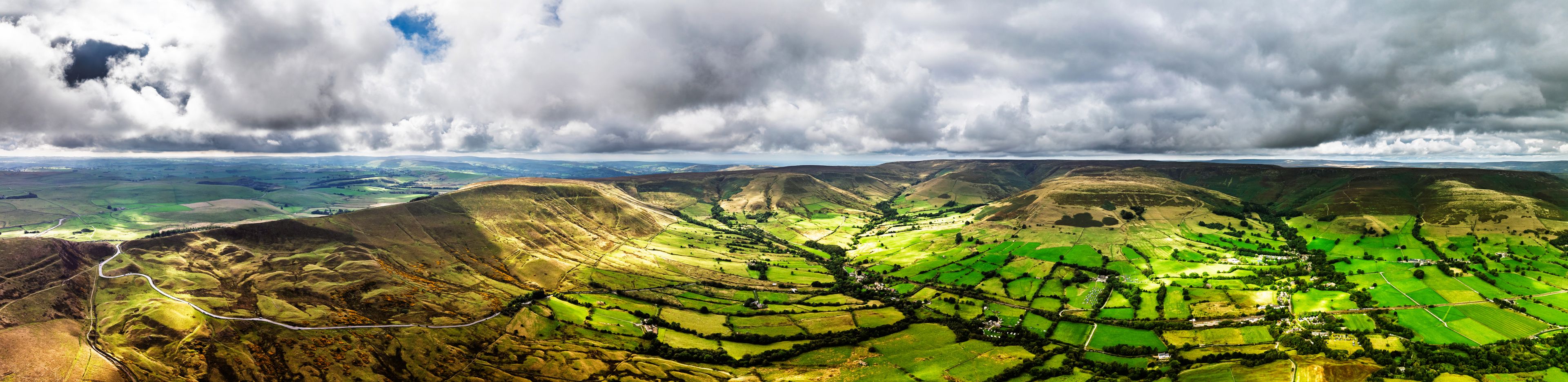 A panoramic view of rolling hills with green fields and a winding road.