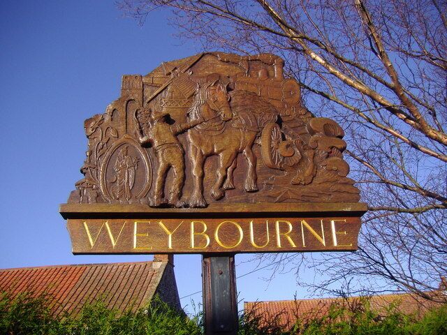 Un letrero de madera con 'WEYBOURNE' y una escena de carruaje tirado por caballos.
