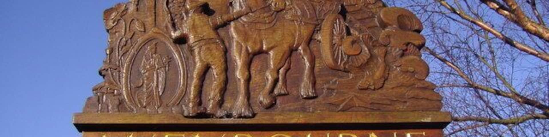 Un letrero de madera con 'WEYBOURNE' y una escena de carruaje tirado por caballos.