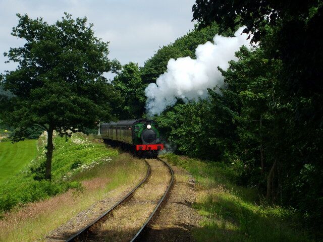 A steam train on a curved track surrounded by lush greenery and trees.