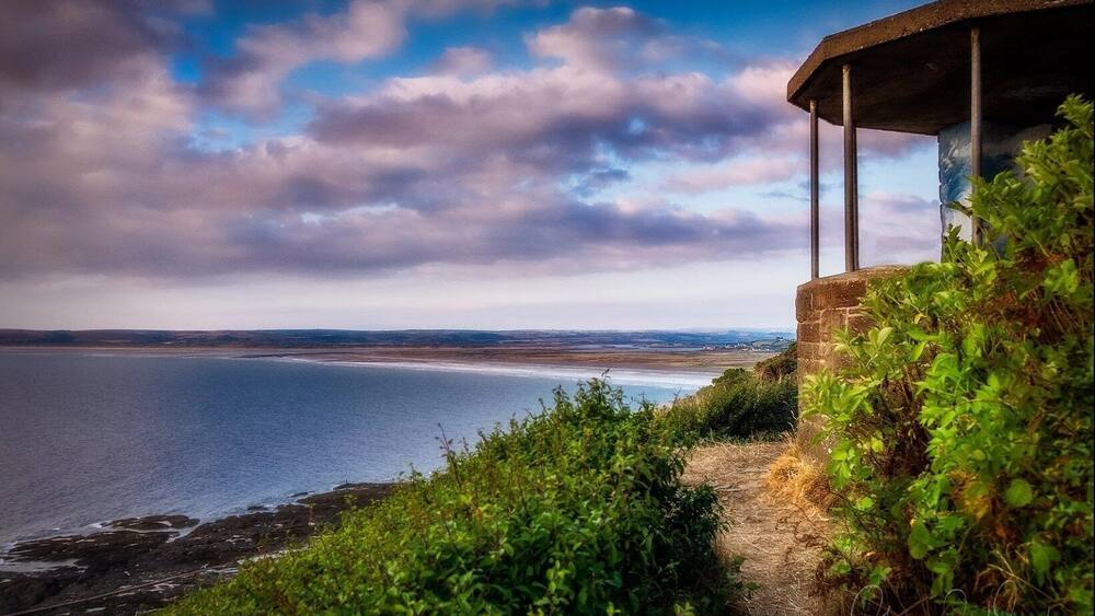 Eine Küstenlandschaft mit einer Steinstruktur mit Blick auf das Meer, umgeben von viel Grün.