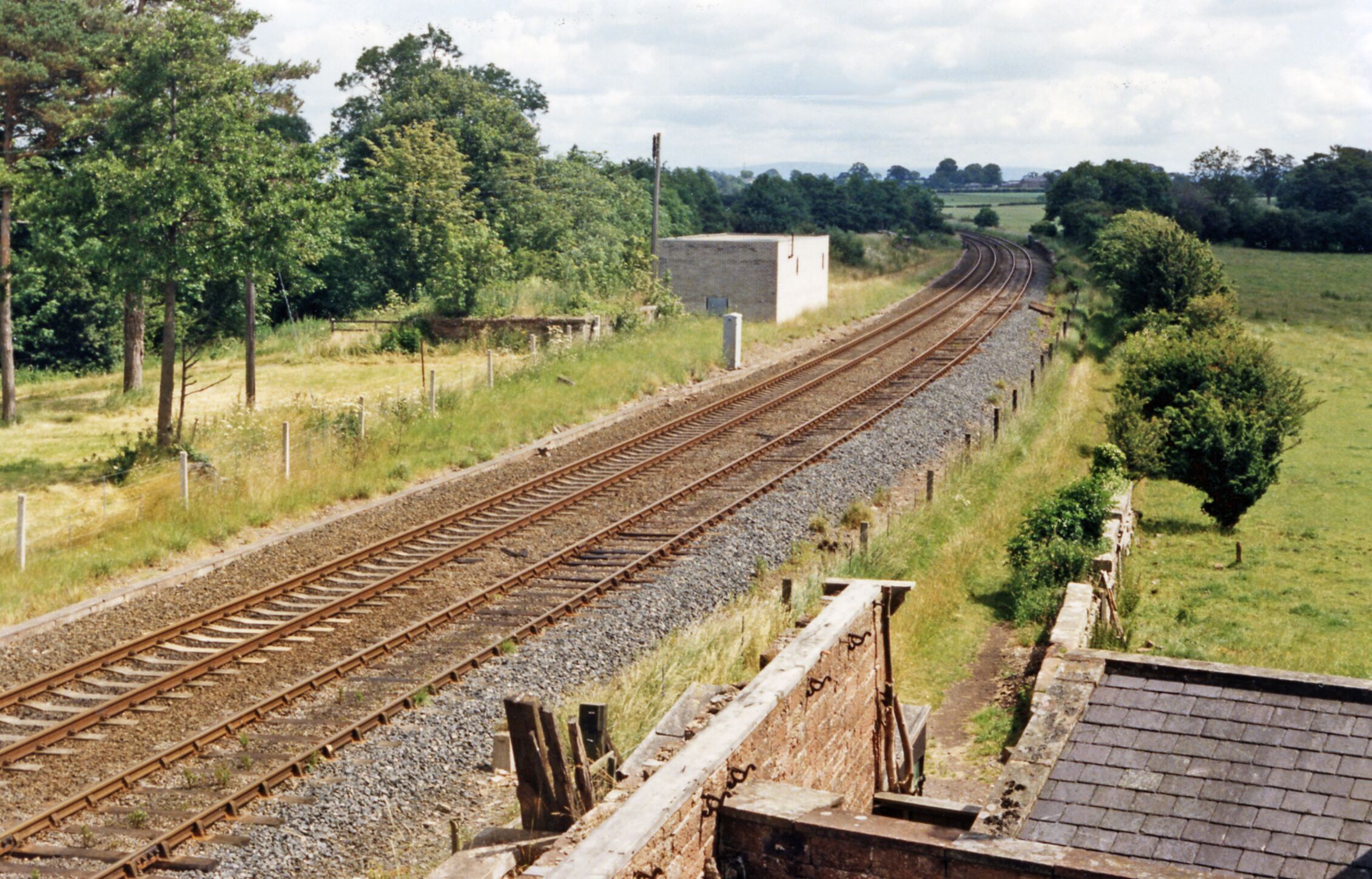Railway tracks curving through a rural landscape with trees and a small building.