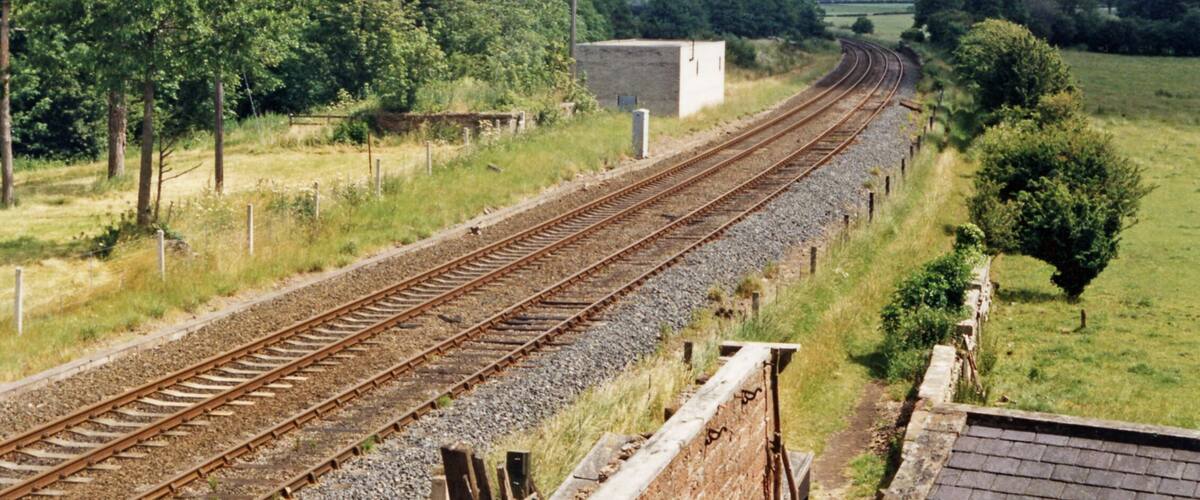 Railway tracks curving through a rural landscape with trees and a small building.