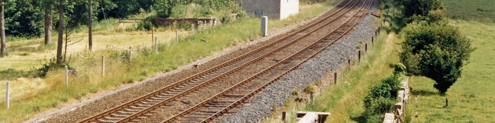 Railway tracks curving through a rural landscape with trees and a small building.