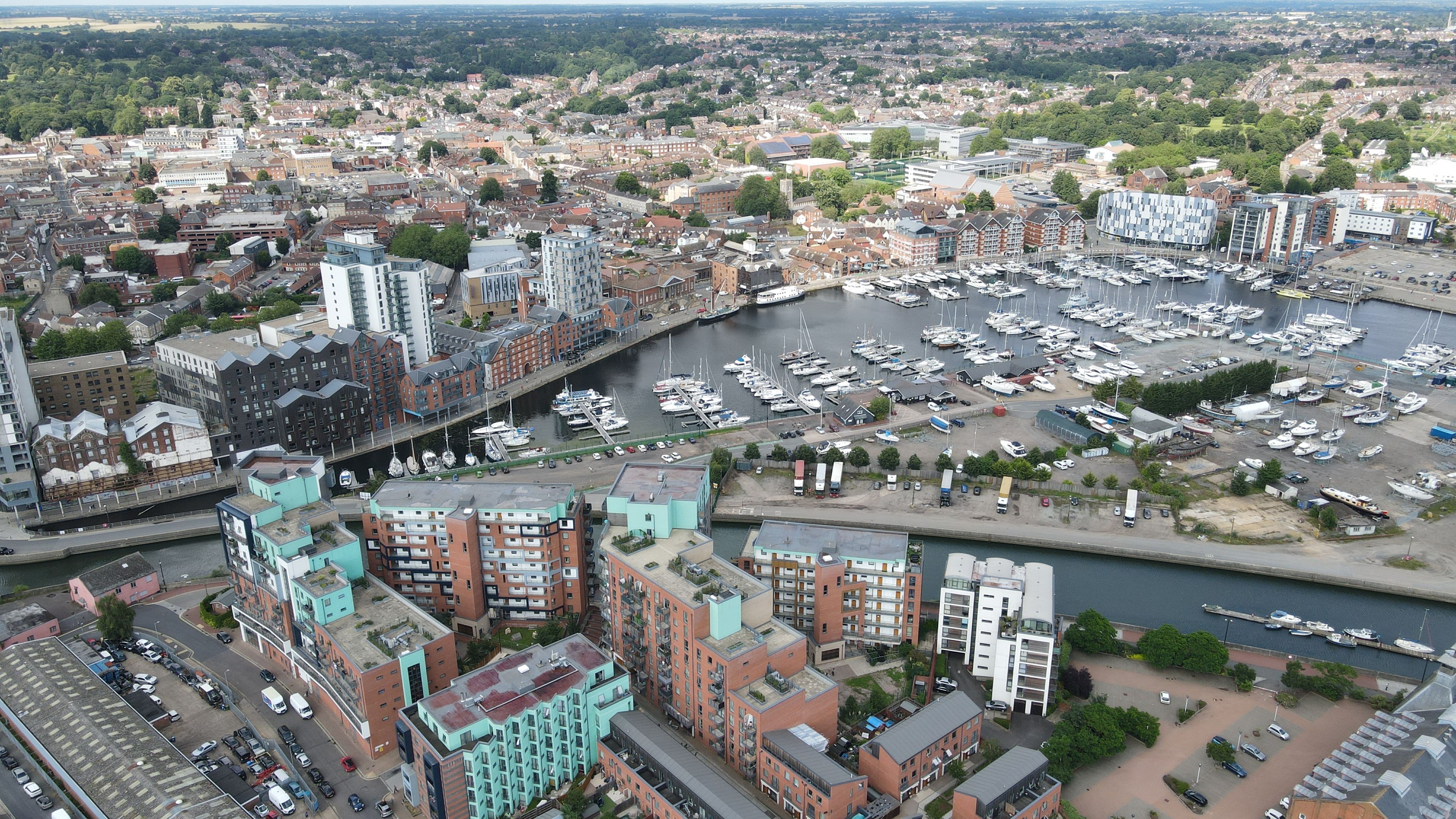 Una marina con numerosos barcos, un río y edificios urbanos circundantes.