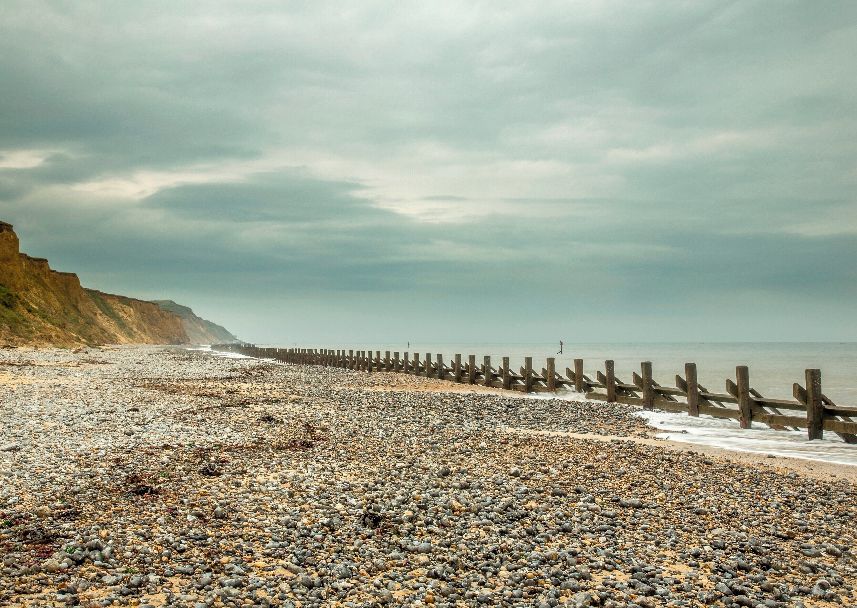 A rocky beach with a wooden sea wall and cliffs in the background.