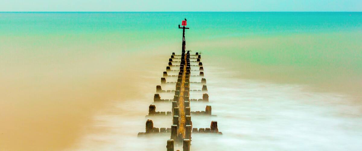 A wooden pier extending into a calm sea with a clear sky.