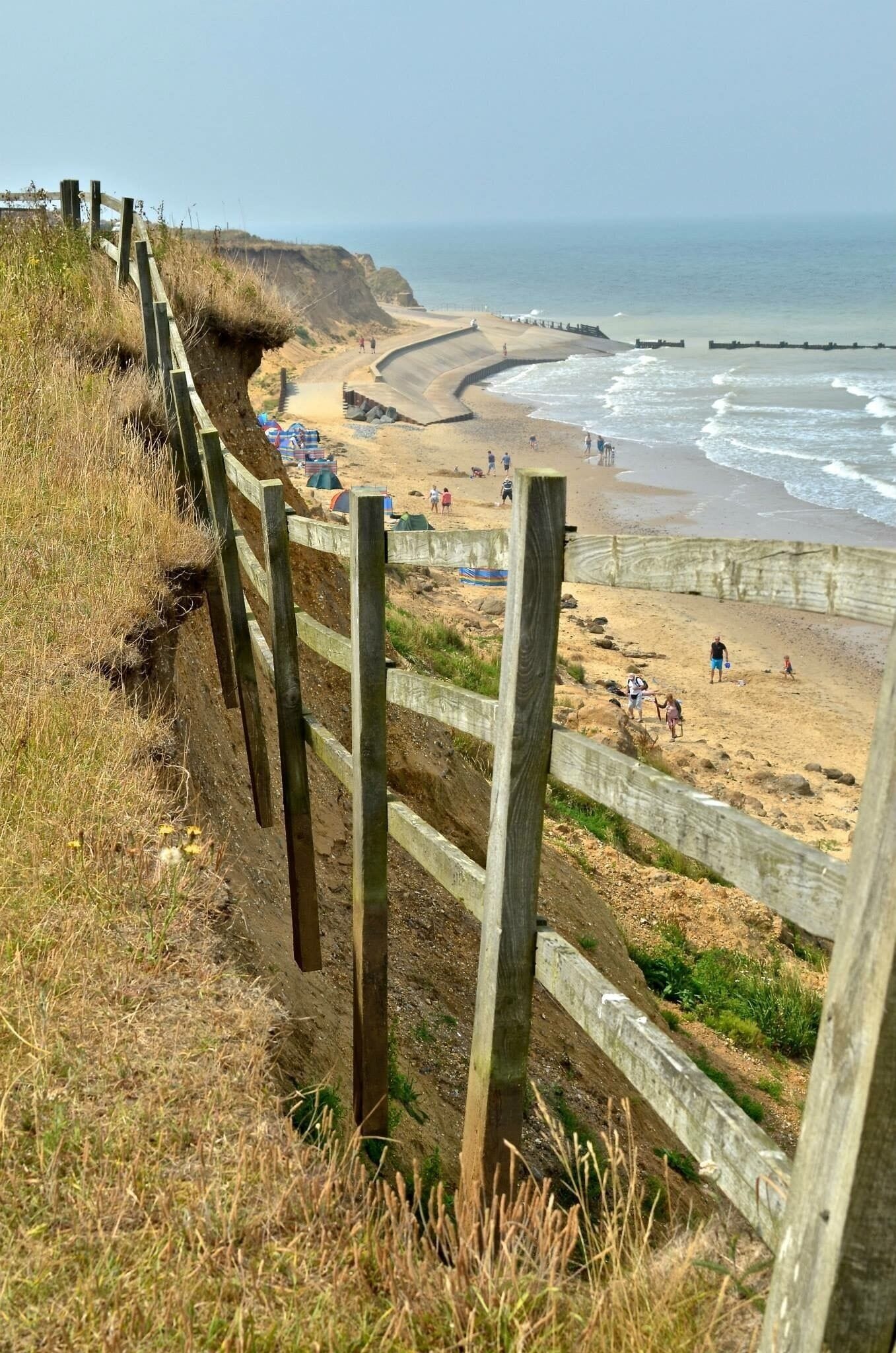 A coastal beach with a wooden fence, sandy shore, and ocean waves.