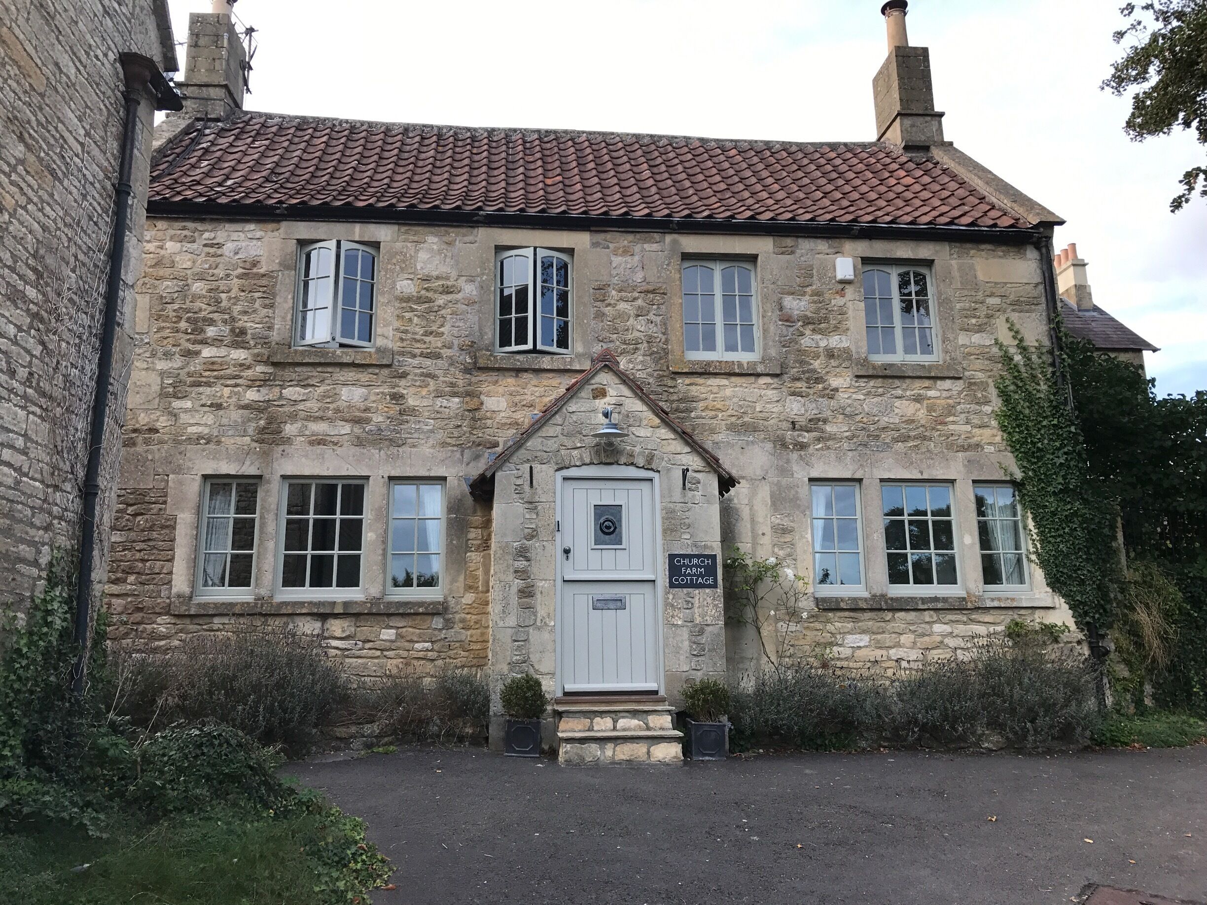 A stone building with a tiled roof, a white door, and a sign reading "CHURCH FARM COTTAGE".