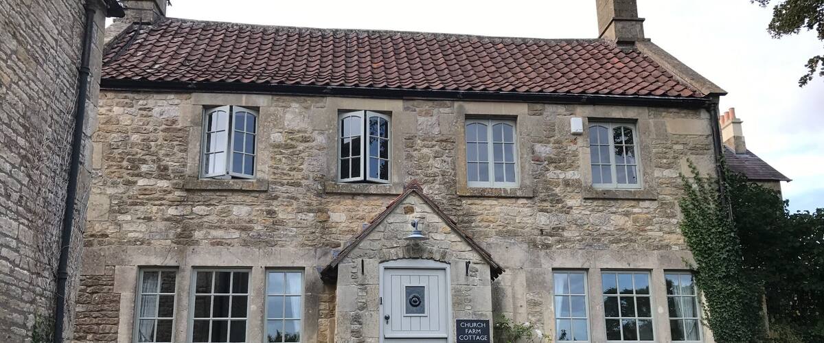 A stone building with a tiled roof, a white door, and a sign reading "CHURCH FARM COTTAGE".