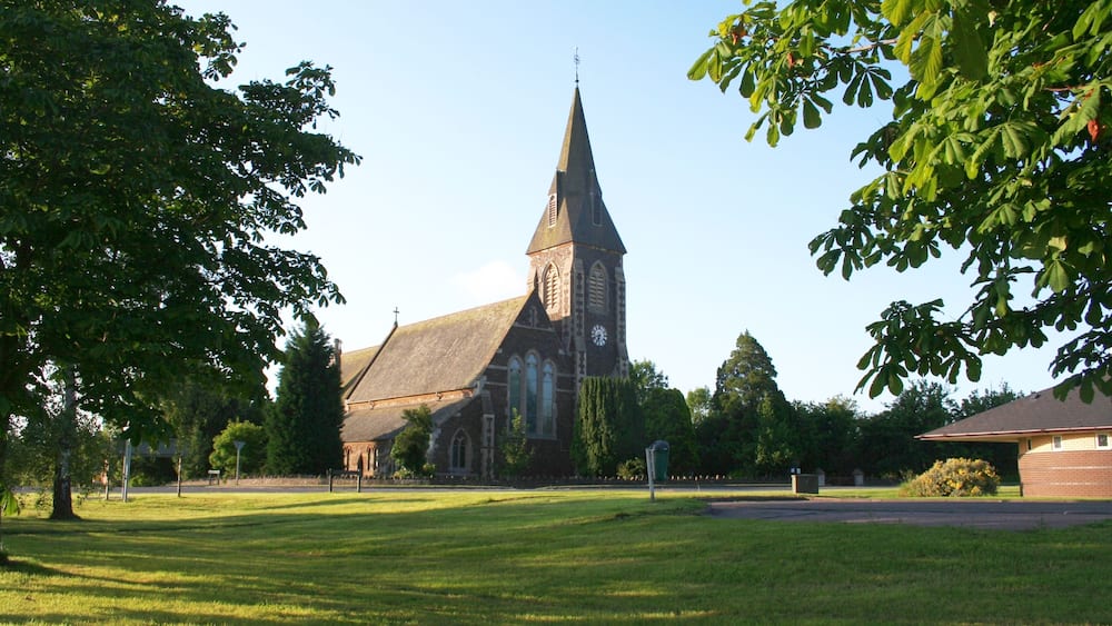 A church with a tall steeple and a clock tower, surrounded by a grassy field and trees.
