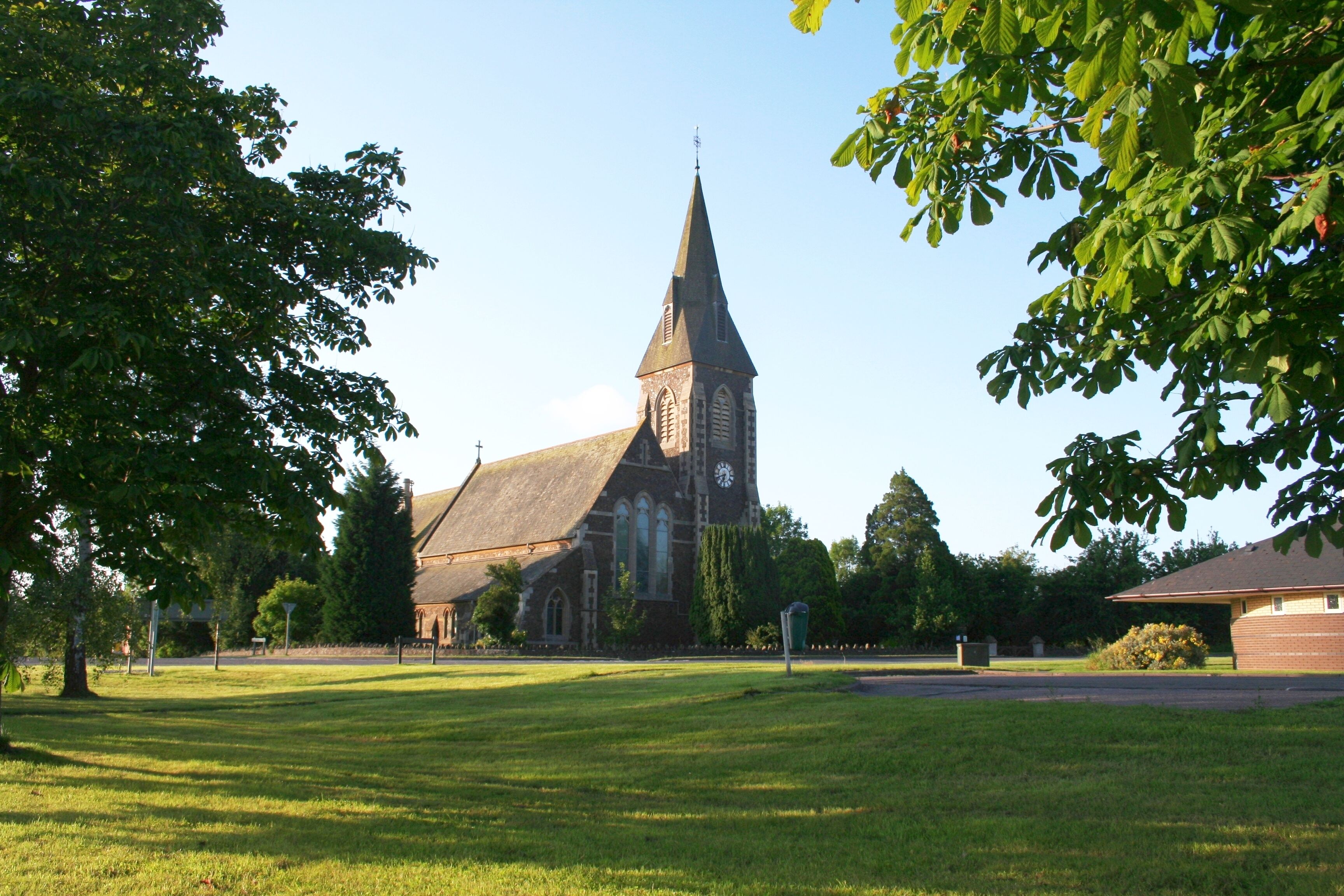 A church with a tall steeple and a clock tower, surrounded by a grassy field and trees.