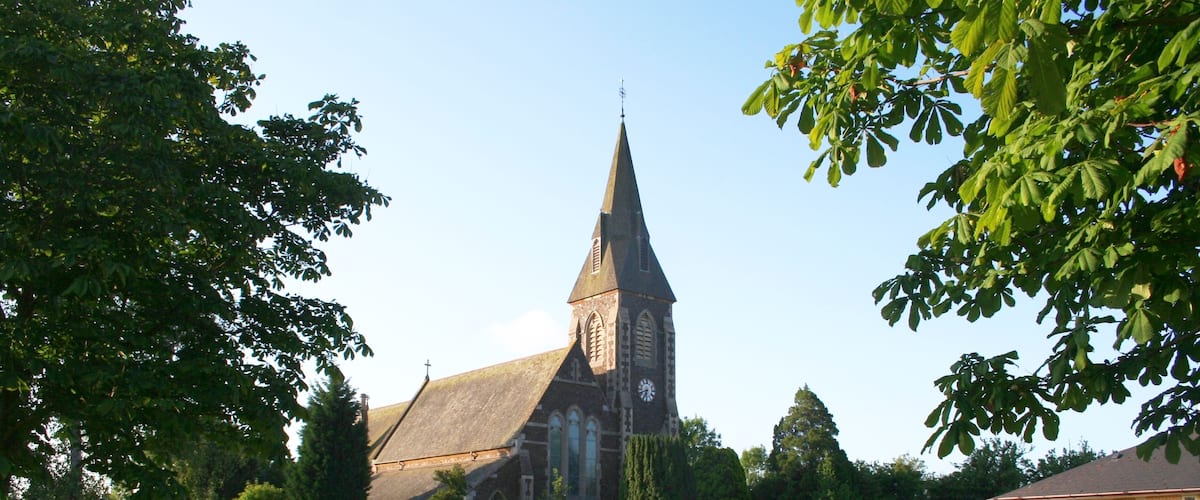 A church with a tall steeple and a clock tower, surrounded by a grassy field and trees.