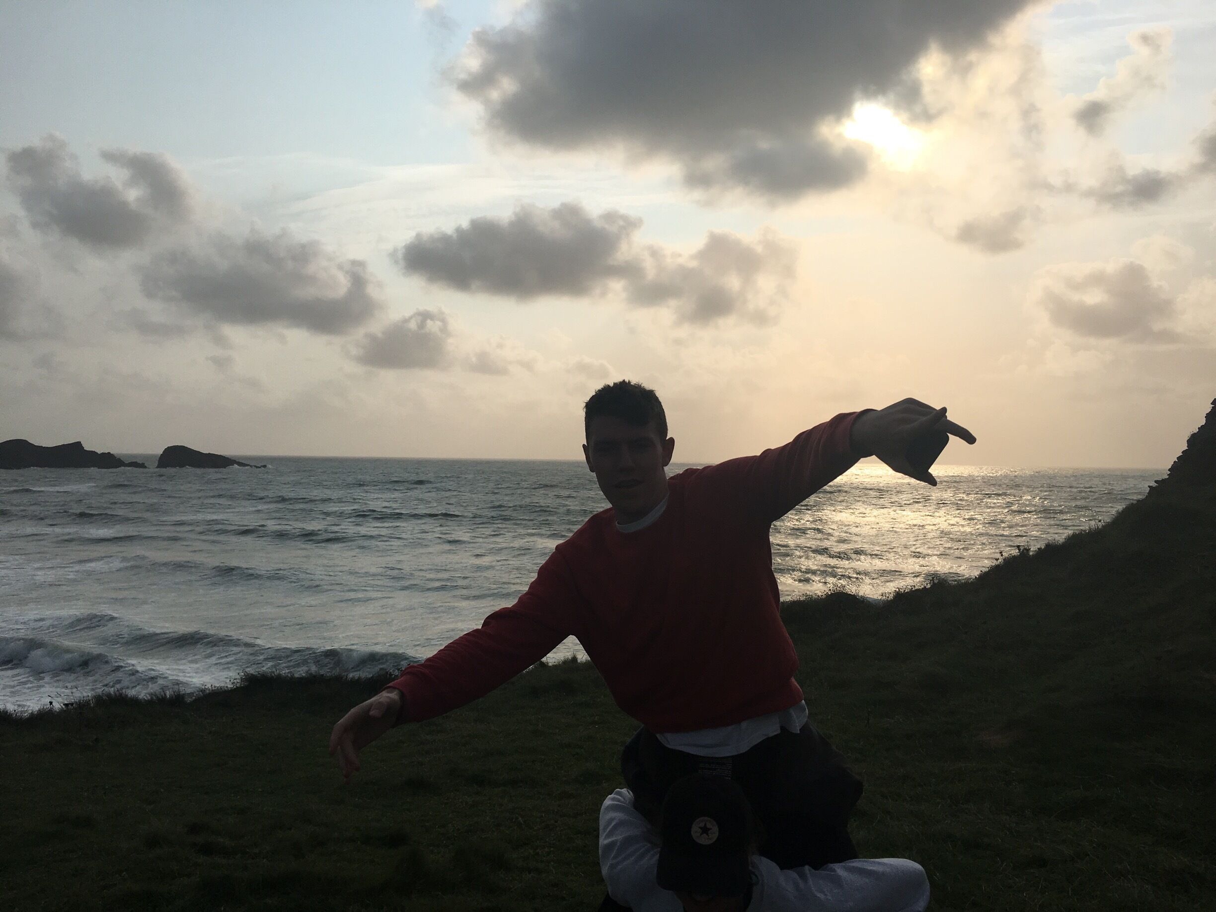 A person standing on a grassy area by the sea with waves crashing onto the shore.
