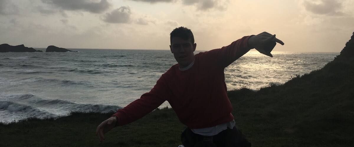 A person standing on a grassy area by the sea with waves crashing onto the shore.
