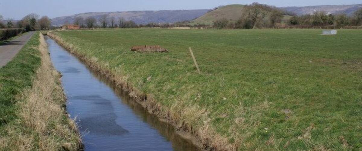 A narrow water channel, a grassy field, and distant hills.
