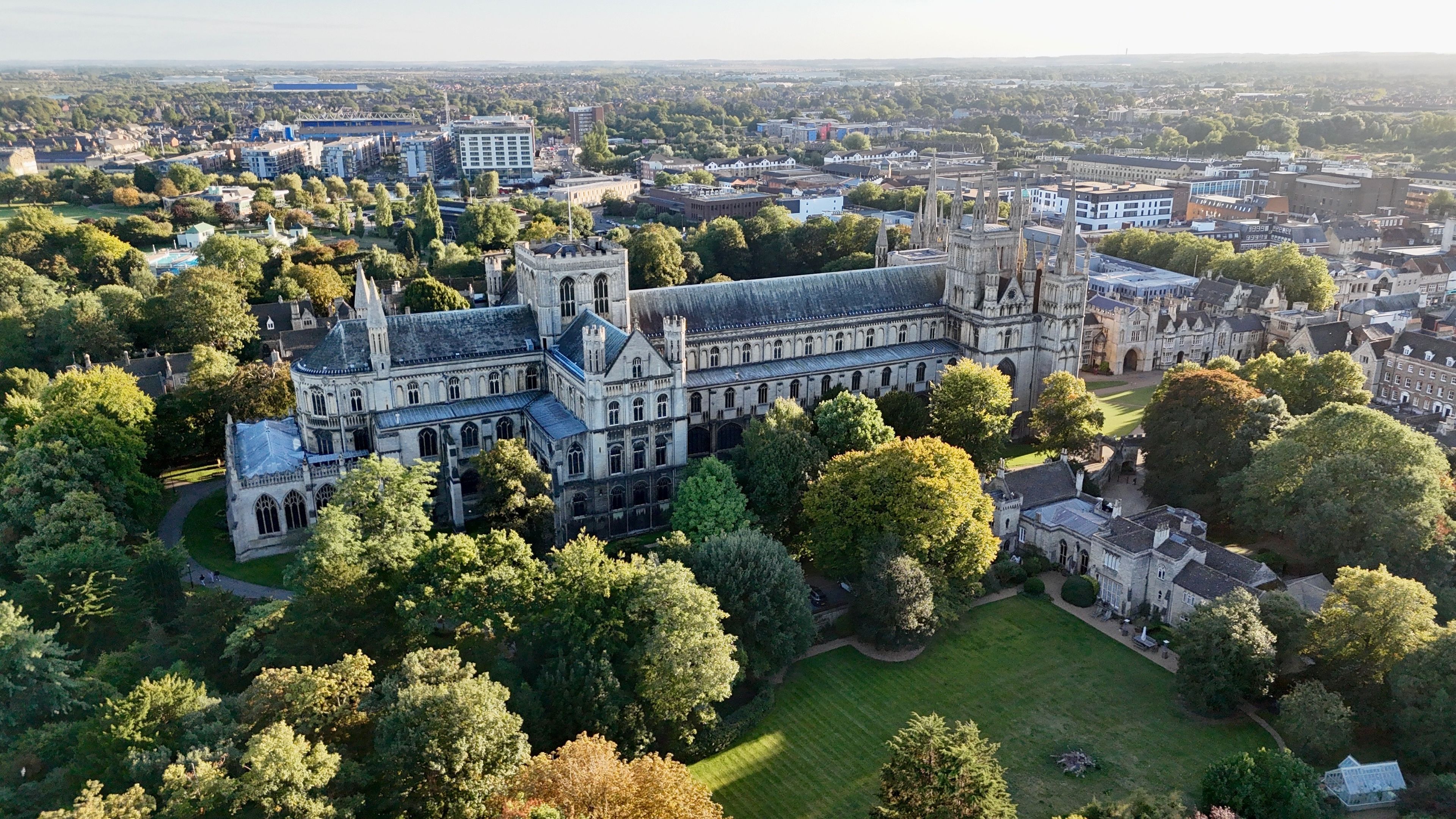 A large historic building with Gothic architecture surrounded by lush greenery and other buildings in the background.