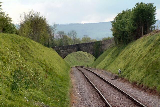 Railway tracks curving through a green landscape with a stone bridge in the distance.