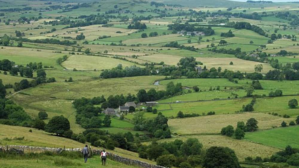 Rolling green hills, scattered houses, and stone walls in a rural landscape.