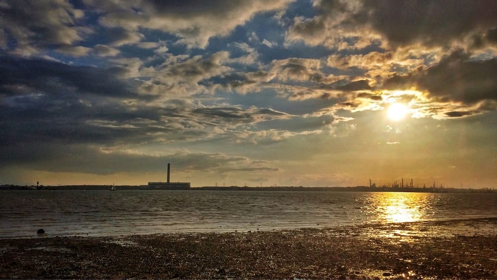 A sunset over a body of water with a distant industrial skyline.