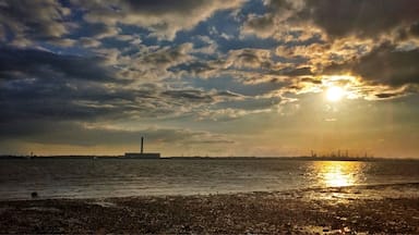 Pôr do sol sobre a água, com um horizonte distante da indústria.