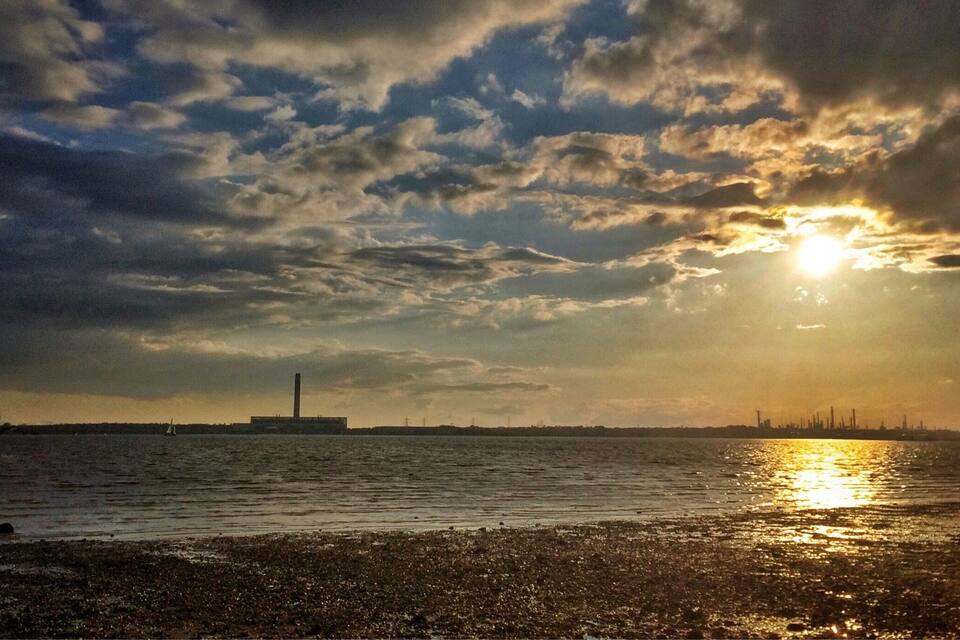 A sunset over a body of water with a distant industrial skyline.