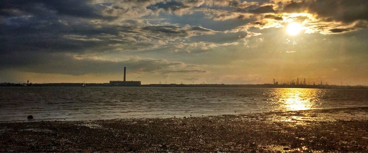 A sunset over a body of water with a distant industrial skyline.