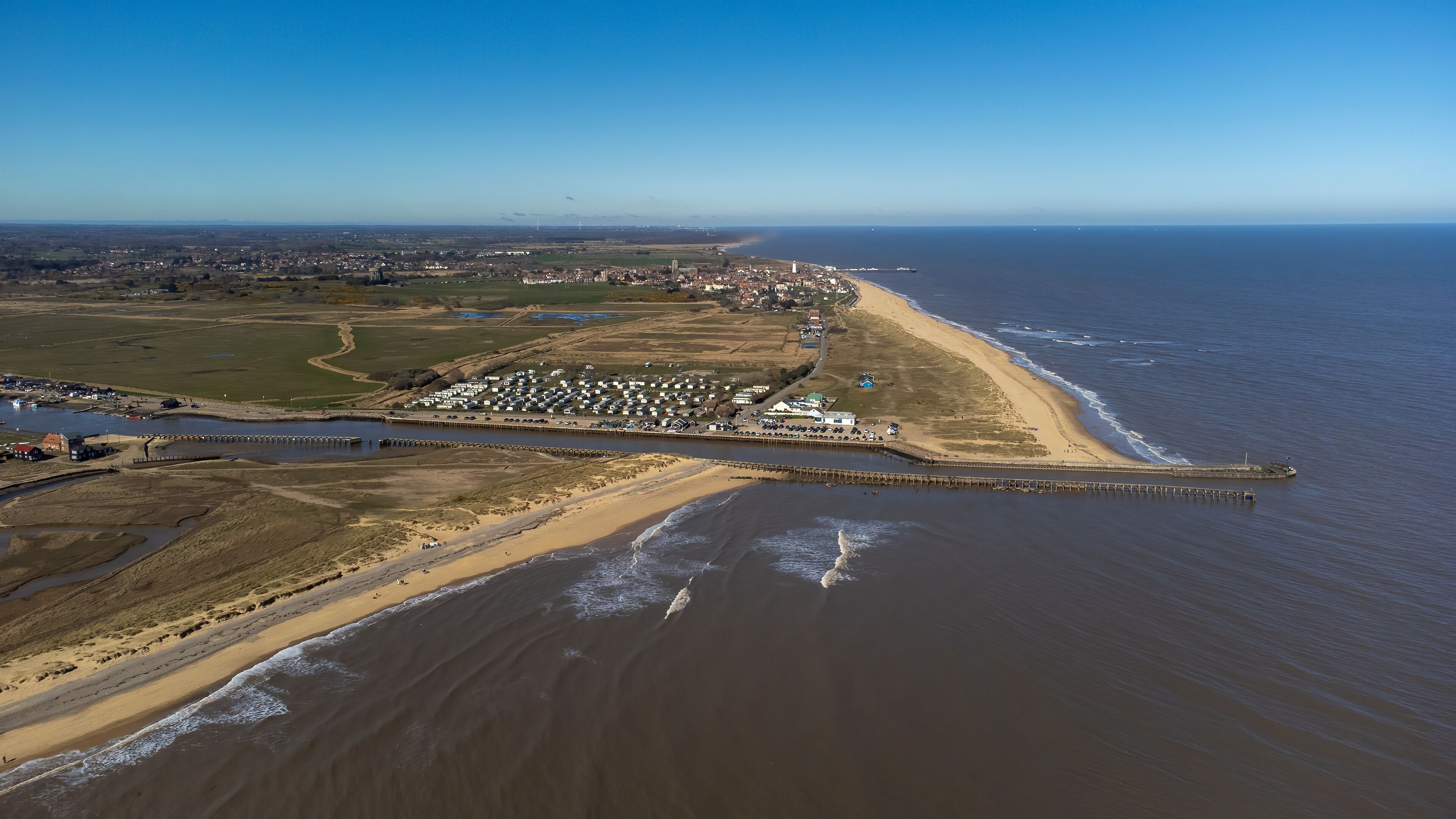 An aerial view of a coastal town with a beach, a pier, and a river.