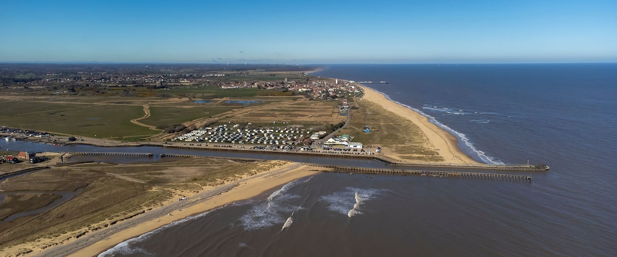 An aerial view of a coastal town with a beach, a pier, and a river.
