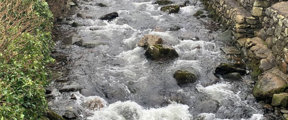 A stone bridge over a fast-flowing river with rocks and greenery around.
