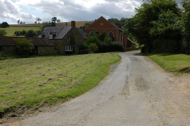 A rural road with a house on the left and a barn in the distance.