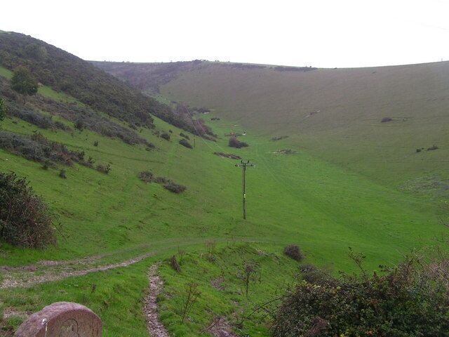 A green valley with a dirt path and a wooden post.