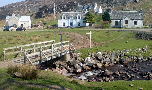 A rural landscape with a stone bridge, a stream, and houses with white walls and grey roofs.