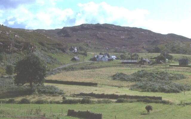 Toscaig. Freshly cut grass lies in a field at Toscaig, while a crofter carries a bundle of hay to dry on the fence in the foreground.