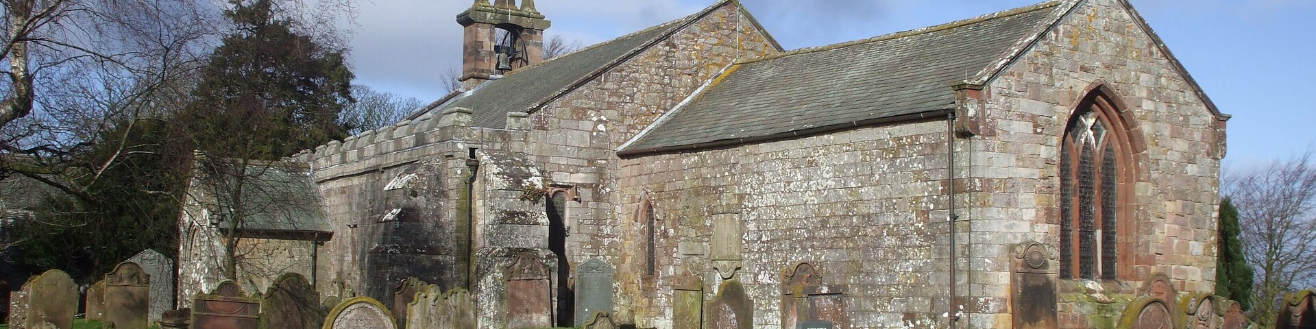 An old church with a bell tower and a graveyard in front.