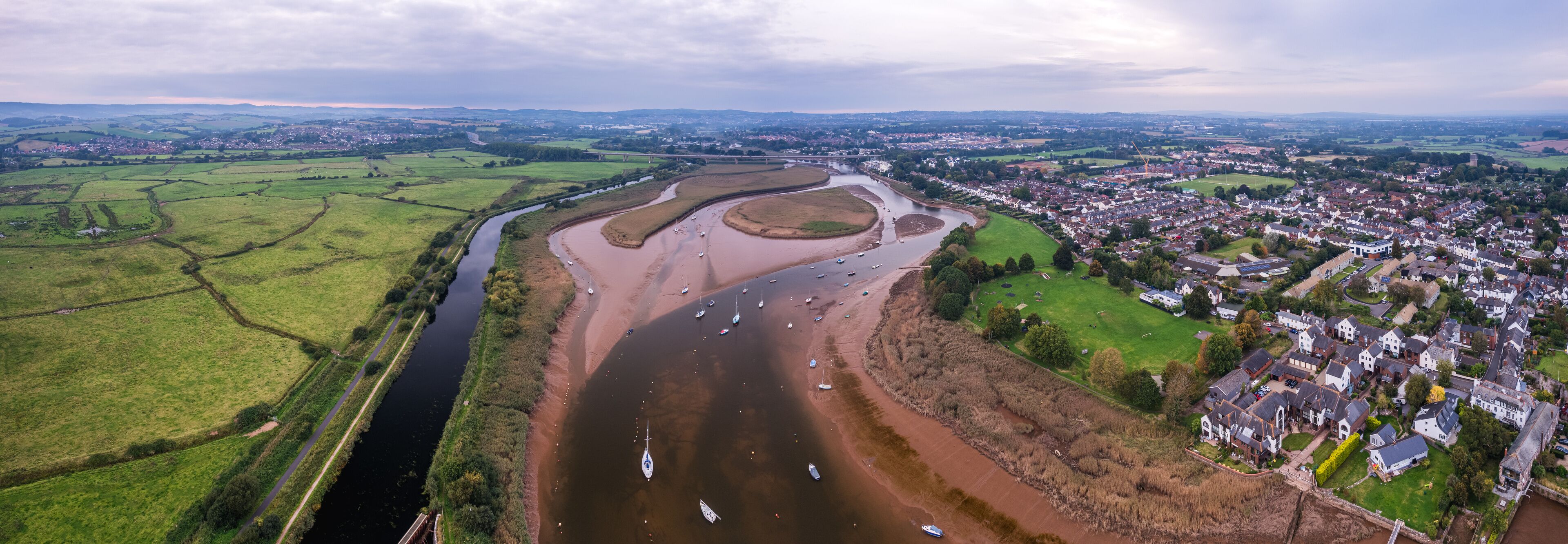 An aerial view of a river meandering through a town with green fields and houses.