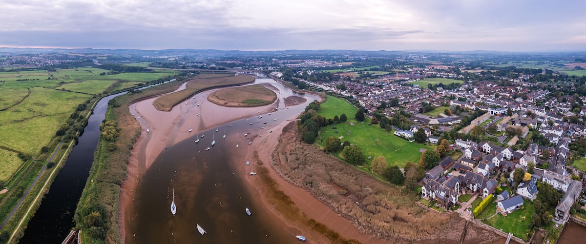 An aerial view of a river meandering through a town with green fields and houses.