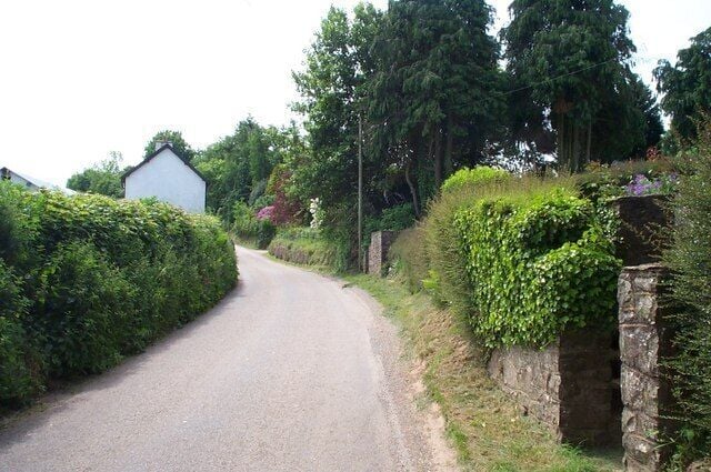 A narrow rural road flanked by stone walls and lush greenery.