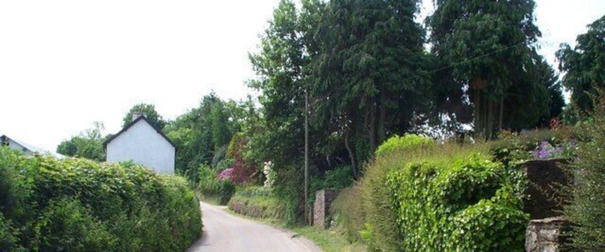A narrow rural road flanked by stone walls and lush greenery.