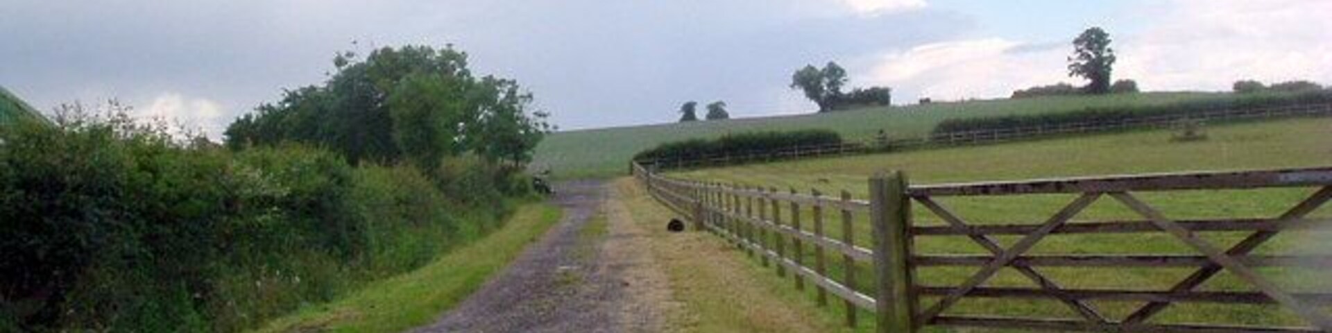A rural road with a wooden gate and a fence.