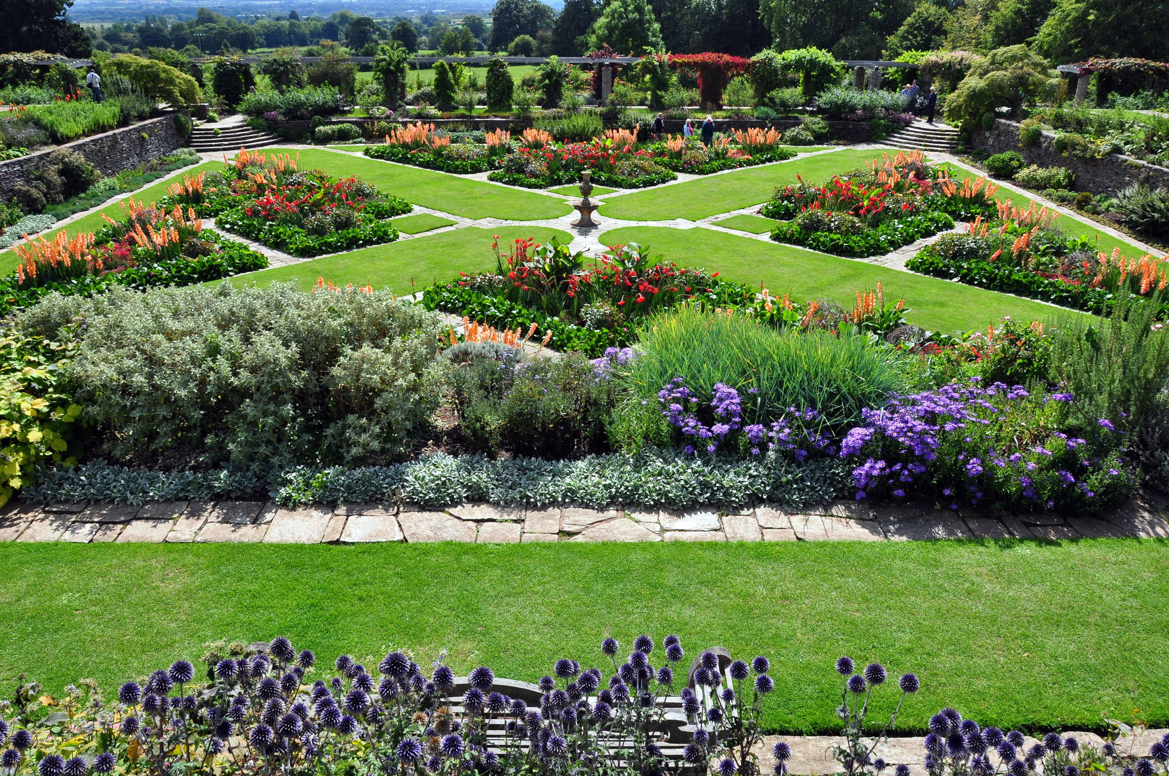 A formal garden with symmetrical flower beds, a central fountain, and a stone pathway.